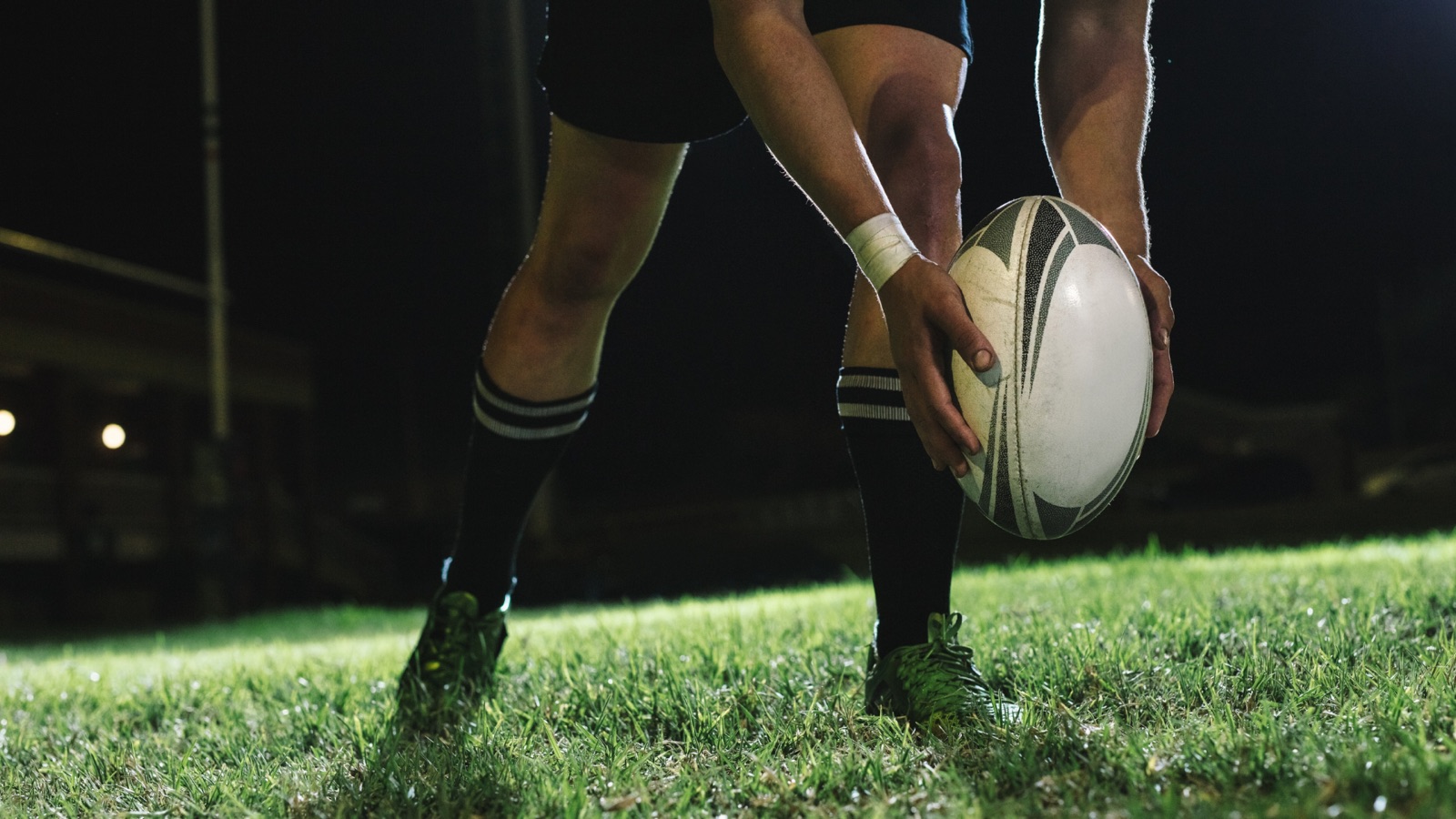 Rugby player placing the ball for a kick under floodlights
